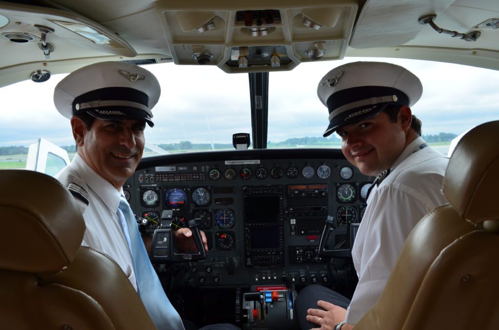 Two pilots in a cockpit at Peachtree DeKalb Airport, looking back and smiling at the camera.