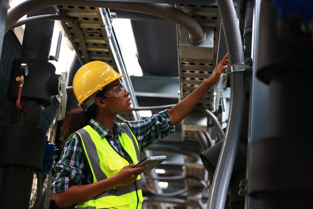 An industrial maintenance technician in a hard hat checking a HVAC system.