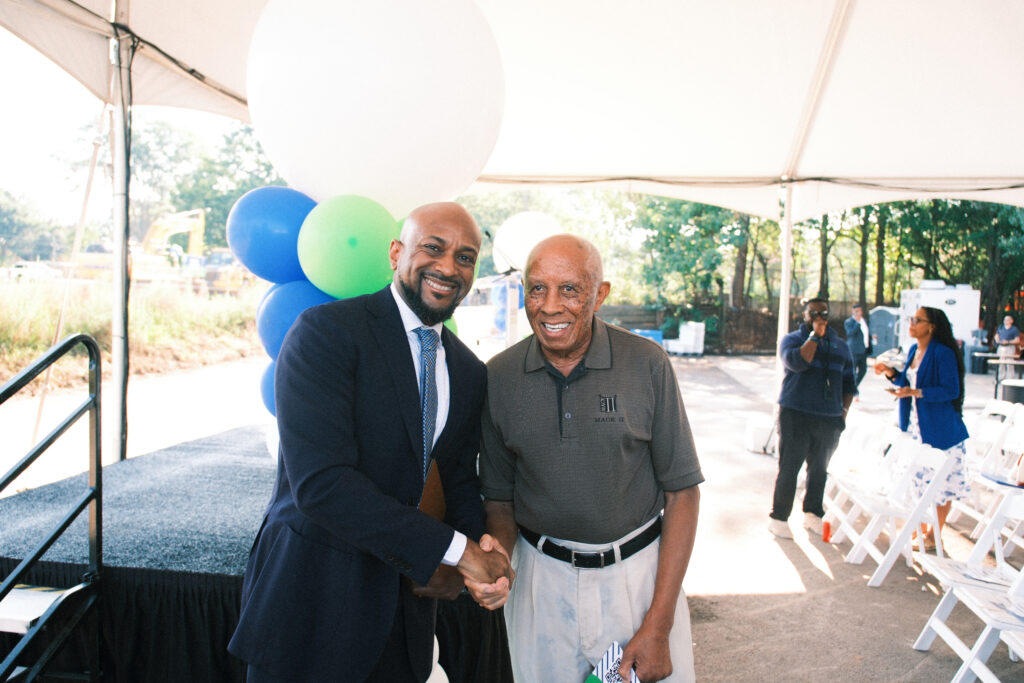 Two men shake hands and smile at the camera.