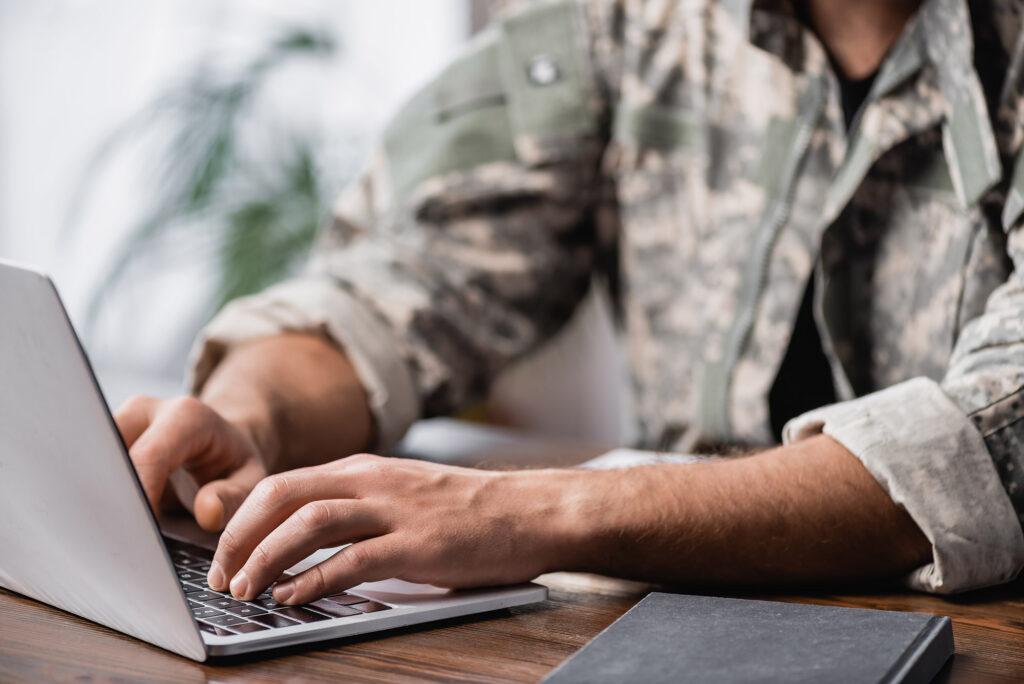 Military man in uniform using laptop on desk.