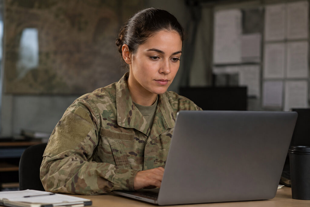 Focused soldier in camouflage uniform working on her laptop.